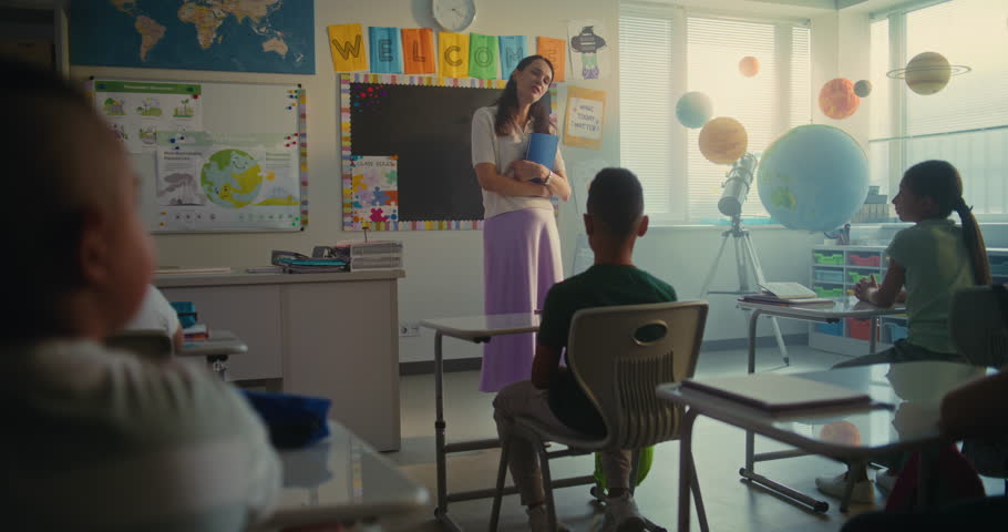 STEM Class: Female Teacher Starting Lesson, Teaching Geography to Primary School Children in Multiethnic Classroom. Group of Young Boys and Girls Sitting at Desks, Learning Science, Listen to Teacher.