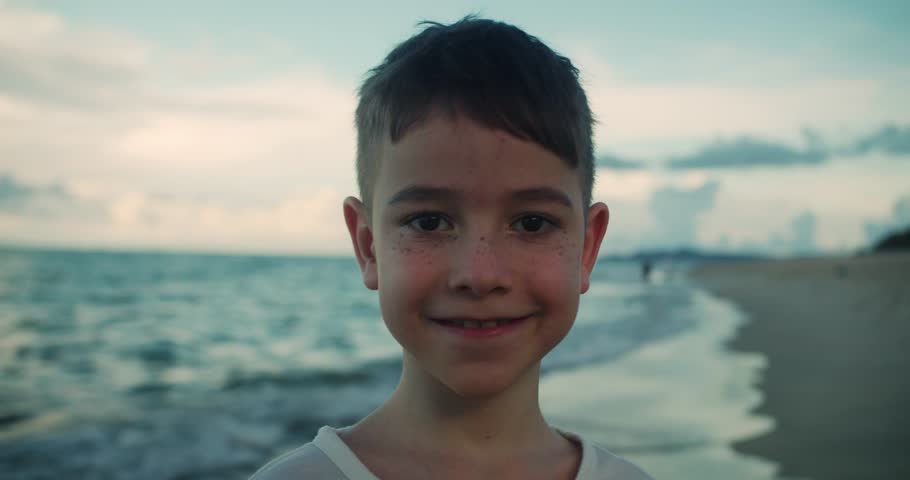 Happy boy 8 to 9 years old smiling close up at the beach. Childhood emotions, summer vacation, and family travel. Joyful kid portrait outdoors by the sea.