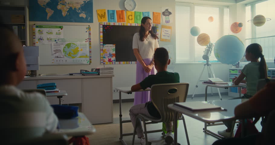 Female Teacher Introducing New Young Student in Front of Class Full of Elementary School Children. Group of Diverse Kids Sitting at the Desks, Clapping in Hands, Greeting New Classmate Before Lesson.