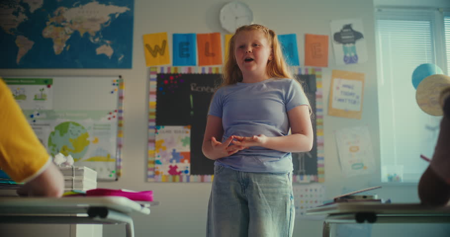 Shy Primary School Girl Showcasing Knowledge of Ecology in Front of Class and Teacher. Smart Kids Sitting at Desks During Environmental Science Lesson in Modern Classroom. STEM Education. Slow Motion.