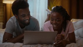 Laughing African American family couple boyfriend man girlfriend woman lying bed having fun laptop computer device online watching comedy funny movie series TV laugh at home illuminated bedroom night - Powered by Shutterstock - Get 15% off with code: PIKWIZARD15