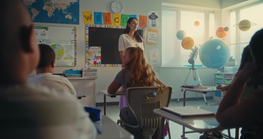 STEM Class on Renewable Energy: Female Teacher Calling Elementary School Student to the Board. Talented Girl Presenting Homework on Ecology in Front of Classroom Full of Diverse Children, Classmates.