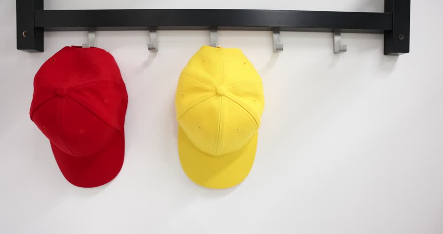 Woman hanging light blue baseball cap onto hook rack on white wall, closeup