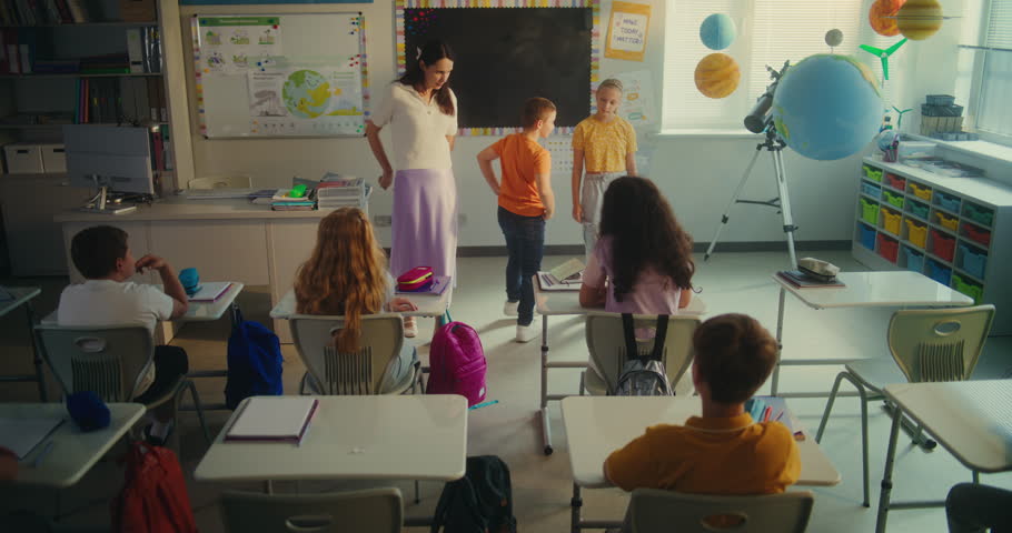 Science Lesson: Primary School Boy and Girl Presenting Homework on Renewable Energy in Front of Class. Female Teacher Educating Ecology to Smart Kids in Modern Classroom. STEM Education. Slow Motion.