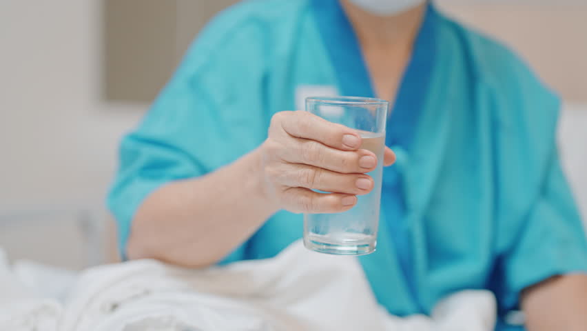 Senior woman with Tremor hand during taking glass of water in hospital. Parkinson disease April awareness month, Carpal Tunnel Syndrome, rheumatoid and brain injury and Neurological disorder concept 