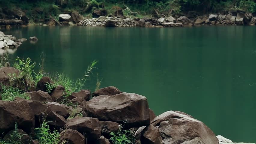 Ambient motion of gentle breeze making minute current in the serene lake, surrounded by rocks and lush greenery. Balinsasayao Twin Lakes Natural Park in Sibulan, Philippines