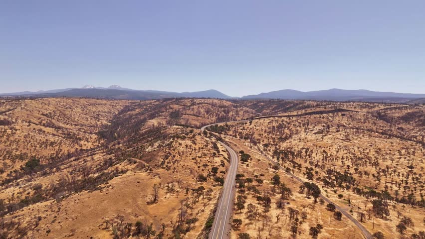 High desert road in California (highway 36), from Red Bluff towards Lassen Volcanic National park, alongside hills with dry grass and small shrubs, early summer	