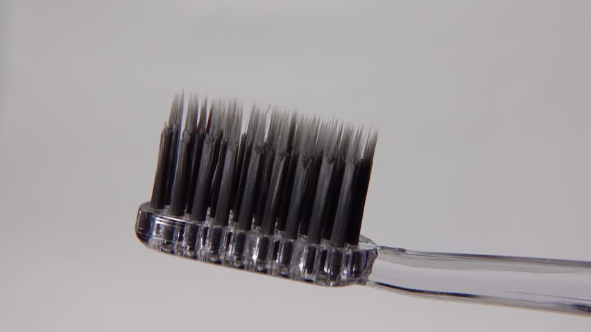 Toothpaste being applied to a black toothbrush against a clean white background, highlighting contrast and modern minimalist hygiene aesthetics.