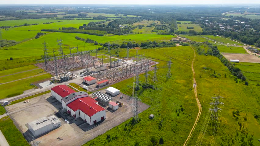 Aerial drone footage flying over a modern electrical distribution power station that powers a data centre or servers next to it at summer sunny day. Large cables and cooling fan systems visible.