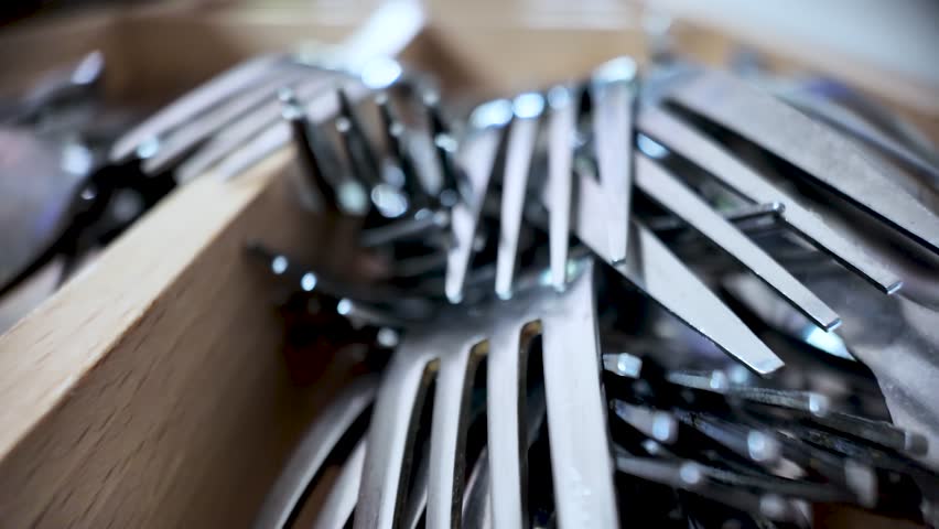 Close-up of metal forks organized in a wooden kitchen cutlery drawer.