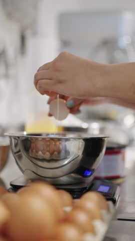 Woman cracking eggs into a stainless steel bowl placed on a kitchen scale