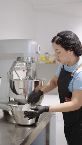 Professional pastry chef pouring a white powder into a metal bowl, using a stand mixer in a modern kitchen