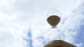 Glass hourglass against blue sky with clouds. Transparent hourglass filled with sand placed against a cloudy blue sky background. Concept of time, transience, waiting, and the passing of life - Powered by Shutterstock - Get 15% off with code: PIKWIZARD15