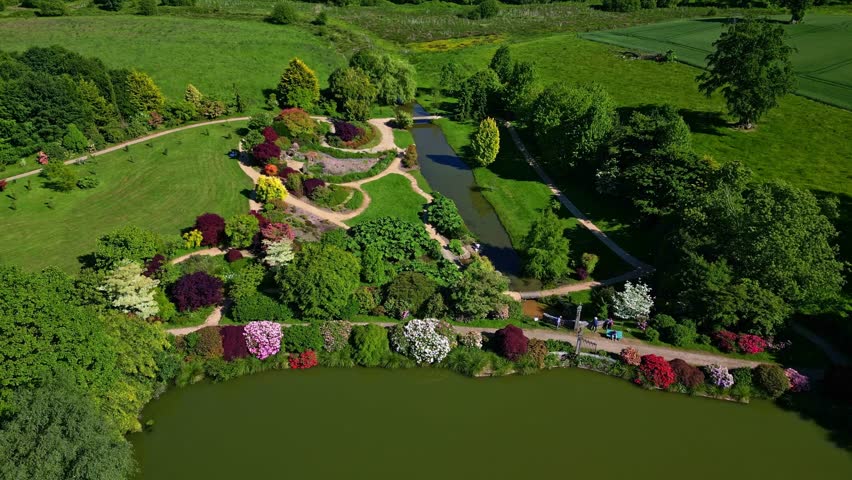 Colorful garden with lake, pond and stream, vibrant flowerbeds, Parc de Haute Bretagne, France. Aerial drone forward descending