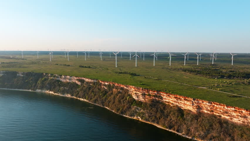 Wind turbines blades in field backdrop of bright orange sunset in sea wind park. Silhouettes of windmills. Alternative energy sources scenic Cape Kaliakra, summer drone image from Bulgaria Black Sea