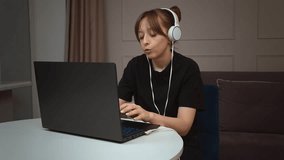 Female freelancer in noise-canceling headphones working remotely on laptop, participating in video calls emotionally and surprised, concentrating on professional task at home workplace - Powered by Shutterstock - Get 15% off with code: PIKWIZARD15