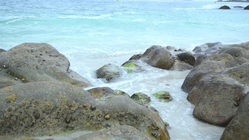 Close-up of small ocean waves gently hitting rocks on the beach. Peaceful, rhythmic motion perfect for themes of nature, relaxation, coastal scenery, and ambient textures.