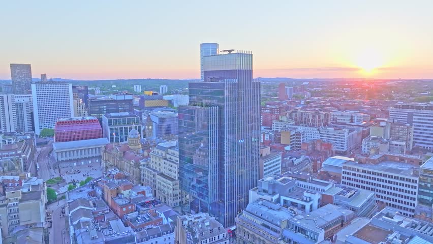 erial footage shows a slow drone ascent above Pigeon Park in Birmingham, featuring the city’s tallest buildings, including 103 Colmore Row and Town Hall, under a glowing sunset.