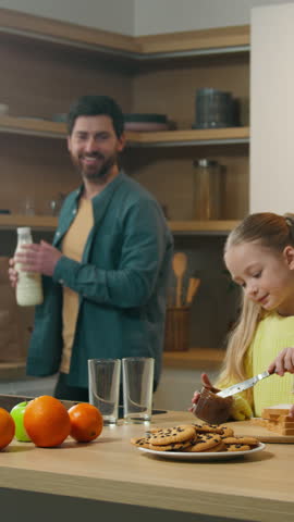 Caucasian family happy cooking breakfast together at kitchen at home mother with little daughter child girl kid prepare toasts bread with chocolate paste father pour milk into glasses cook delivery