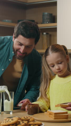 Caucasian family happy cooking breakfast together at kitchen at home mother with little daughter child girl kid prepare toasts bread with chocolate paste father pour milk into glasses cook delivery