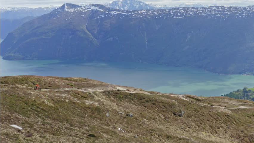 Epic mountain biking adventure above the fjords near Sogndal, Norway. Rider tackles rugged trails surrounded by dramatic cliffs, lush green hills, and stunning Nordic scenery.