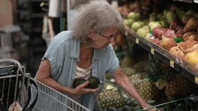 An elderly senior woman carefully chooses fresh avocados from a grocery store display filled with various fruits, showcasing her dedication to healthy eating. - Powered by Shutterstock - Get 15% off with code: PIKWIZARD15