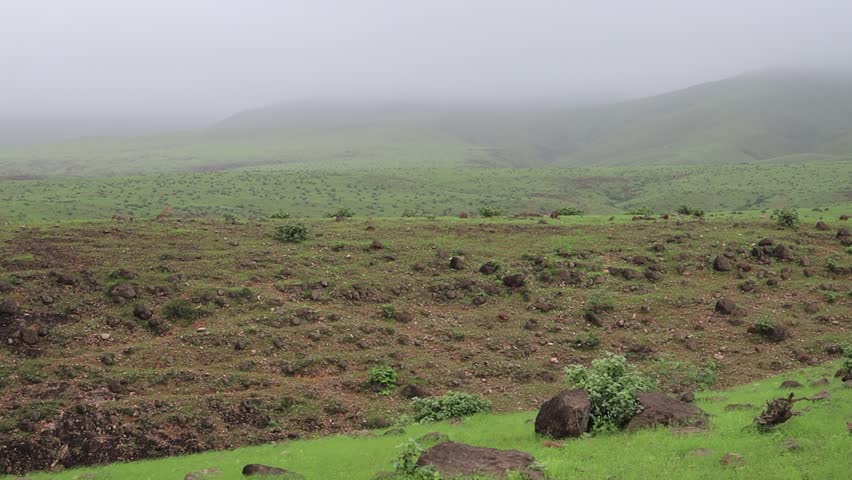 An aerial view of lush green grass and scattered rocks in a Salalah valley, Oman, captured during the cloudy and misty Khareef monsoon season