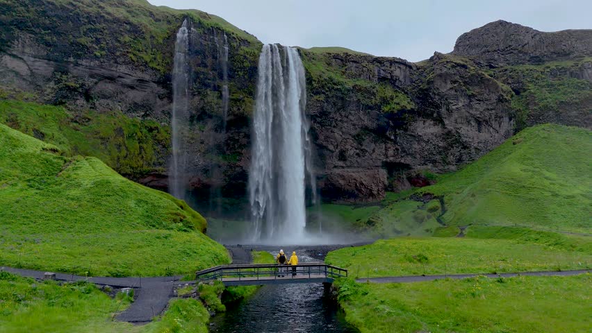A couple stands on a bridge near the magnificent Seljalandsfoss waterfall in Iceland.