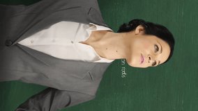 Animation of a young Caucasian woman holding a calculator and notebook, looking around and smiling to camera. Behind her is a green chalkboard with moving mathematical graphs and formulae written in - Powered by Shutterstock - Get 15% off with code: PIKWIZARD15