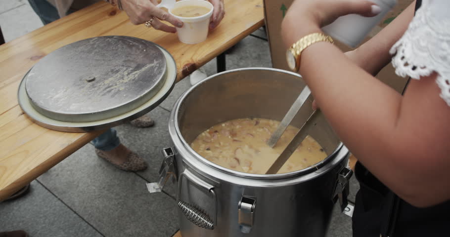 Serving traditional Polish pea soup (grochówka) from a field kitchen thermos during a public event. A person