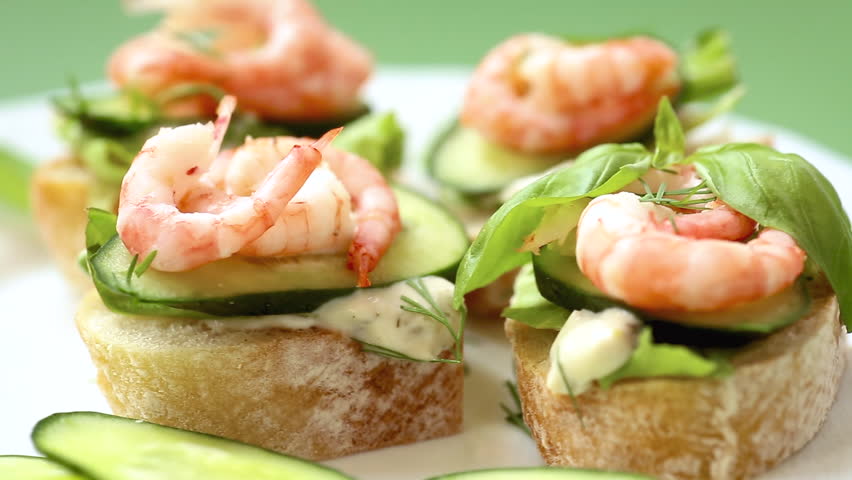 Small canapes with shrimps, salad and cucumbers on a green background.