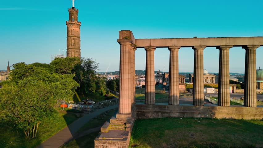 An aerial perspective capturing the iconic Calton Hill with its historic monuments. The sun sets over Edinburgh, casting a warm glow over the cityscape.