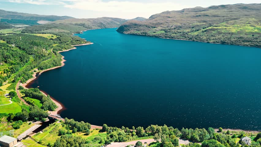 Lush green hills frame the deep blue waters of Loch Lomond, creating a serene landscape. This aerial perspective captures the beauty of nature in Scotland.