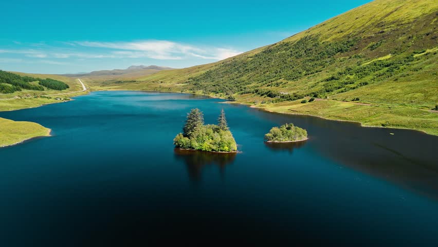 Vibrant green hills frame a tranquil lake with small islands. Clear blue skies reflect on the water, creating a serene atmosphere perfect for nature lovers.