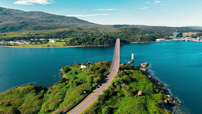 An aerial perspective captures a bridge spanning over tranquil waters, surrounded by lush greenery and mountains, highlighting the natural beauty of Scotland’s coastline.