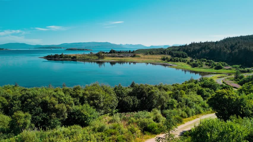Bright blue waters reflect the clear sky while lush greenery lines the shore. The tranquility of the Scottish landscape invites exploration and relaxation.