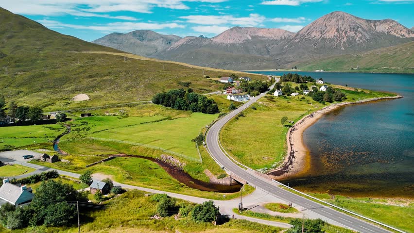 Breathtaking landscape in Scotland featuring a winding road by a tranquil lake surrounded by green hills and mountains under a clear blue sky.