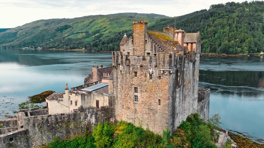 Eilean Donan Castle stands majestically by the loch, surrounded by serene waters and lush hills of Scotland, showcasing its historical architecture and natural beauty.