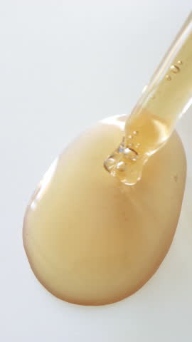 Facial serum texture dispensed from dropper onto white background, close-up. Golden gel texture vitamin C serum with air bubbles, clean beauty, product ingredients, cosmetics