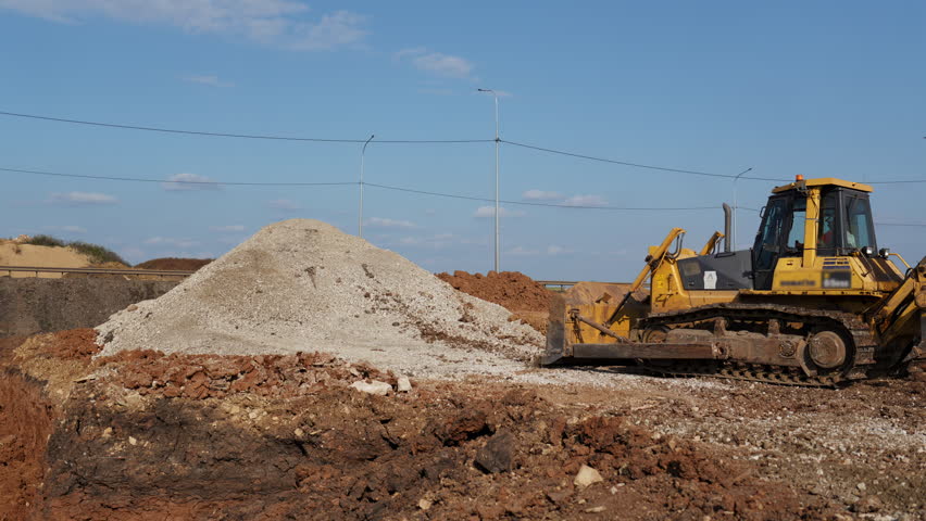 Bulldozer moving gravel on construction site under blue sky. Clip
