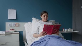 Young adult pregnant patient lying in comfortable hospital bed while reading aloud book about Christmas - Powered by Shutterstock - Get 15% off with code: PIKWIZARD15