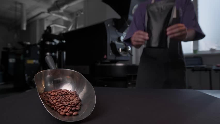 Coffee roasting process in factory, worker places pack of packaged fresh beans to table.