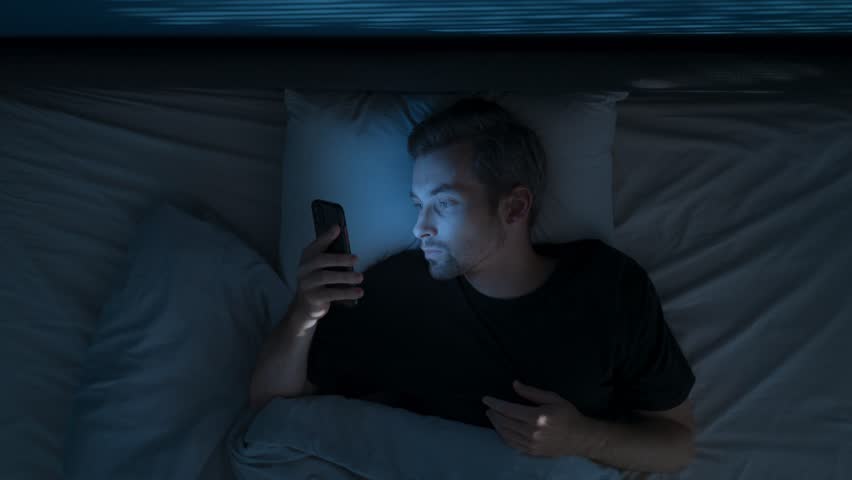 Time lapse, top view, a man uses his smartphone for a long time at night, scrolling through feeds and hanging out on social media instead of sleeping. Digital addiction