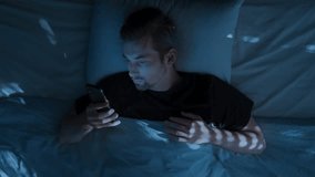 Top view, young man laying in bed at night, holding smartphone and doom scrolling through social media, then tossing the phone aside in exhaustion and frustration. Smartphone addiction and insomnia - Powered by Shutterstock - Get 15% off with code: PIKWIZARD15