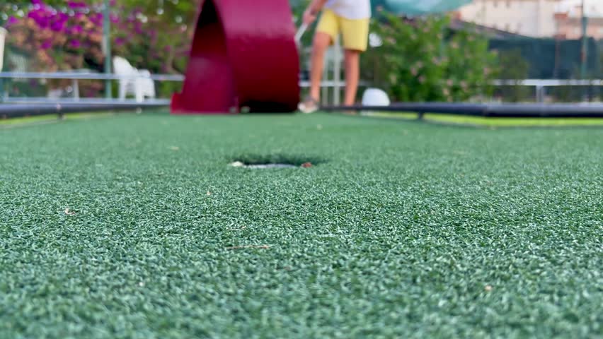 Child playing mini golf, learning through trial and error, eventually scoring a point