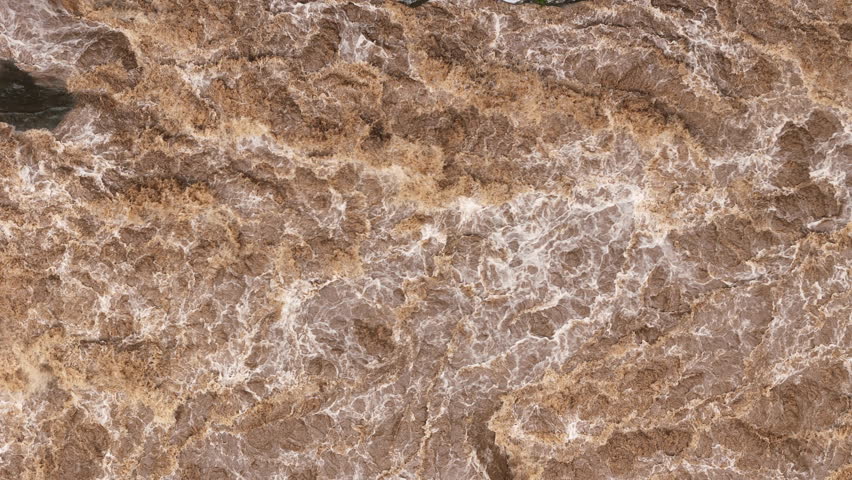 High-pressure flood water in mountain river tributary. A mountain river or stream raging in a flash flood. Upstream view over the turbulent waters.