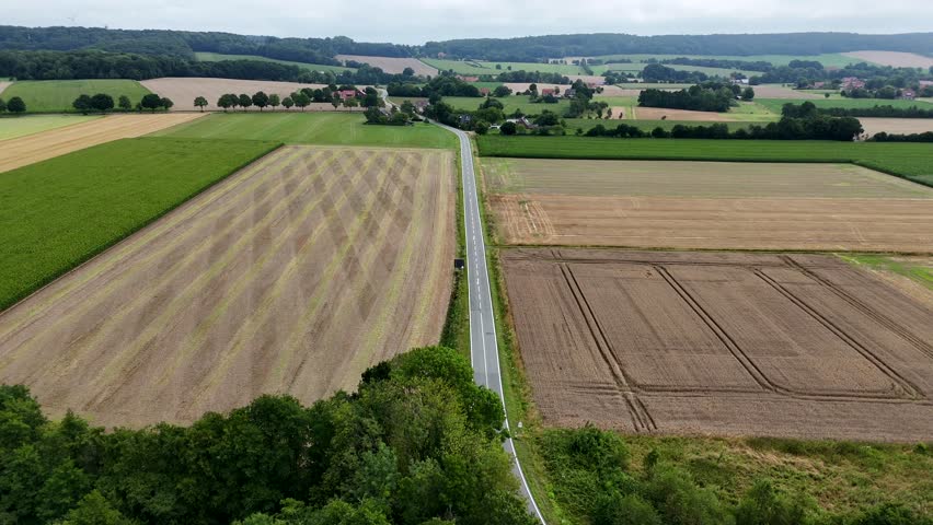 Main Street surrounded by agricultural farm fields and hills on cloudy summer day. American rural suburbia area. Aerials forward wide shot. Quiet and quaint landscape in United States.