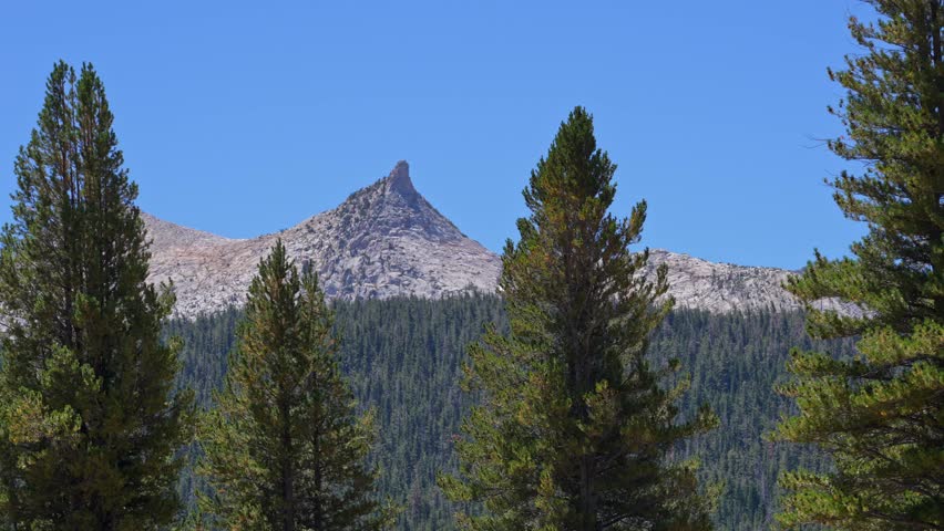 Static 4K shot frames Cathedral Peak, a jagged granite mountain in Yosemite National Park, centered against a clear blue sky.