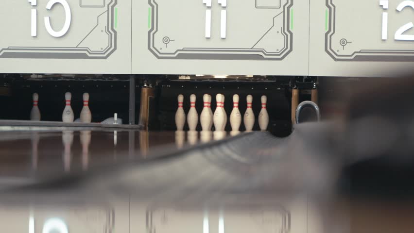 Asian person in casual outfit rolls a bowling ball smoothly on the lane toward the pins, captured indoors with clear background, showing focus, motion, and game preparation