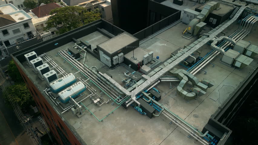 Detailed top-down view of rooftop HVAC layout including air conditioning units, tanks, ducting and insulated piping. Urban engineering solution for climate control on high-rise building.
